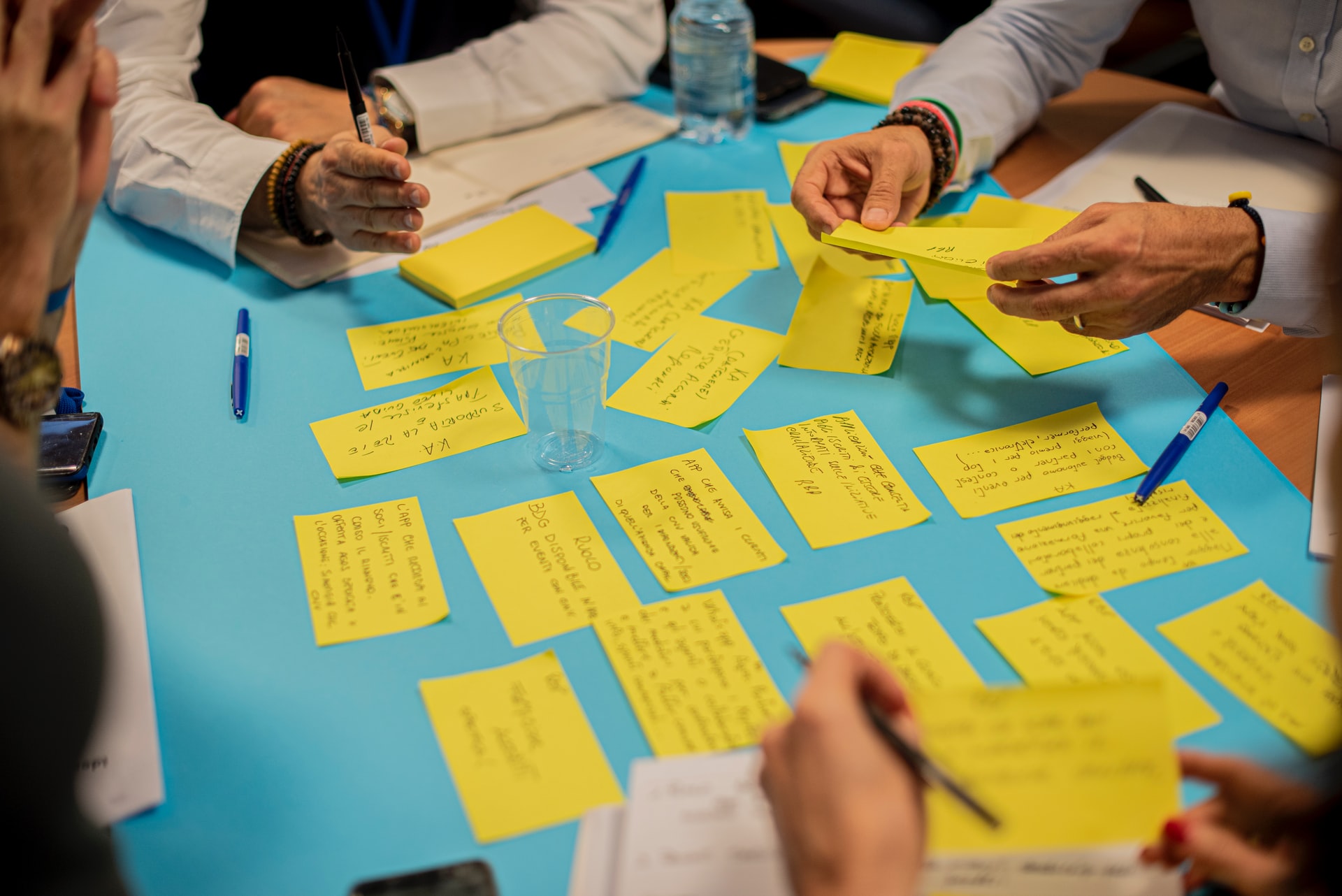 Multiple people writing on yellow notes, with multiple yellow notes already laid out on the table